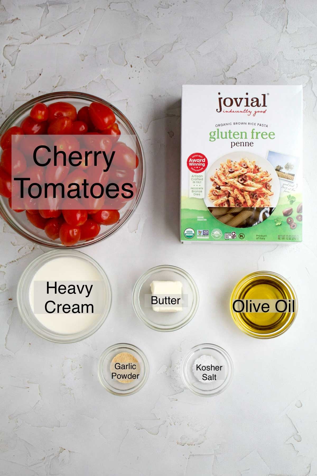 Cherry tomato pasta ingredients in separate containers: cherry tomatoes, jovial gluten free penne pasta, heavy cream, butter, olive oil, garlic powder, and kosher salt.