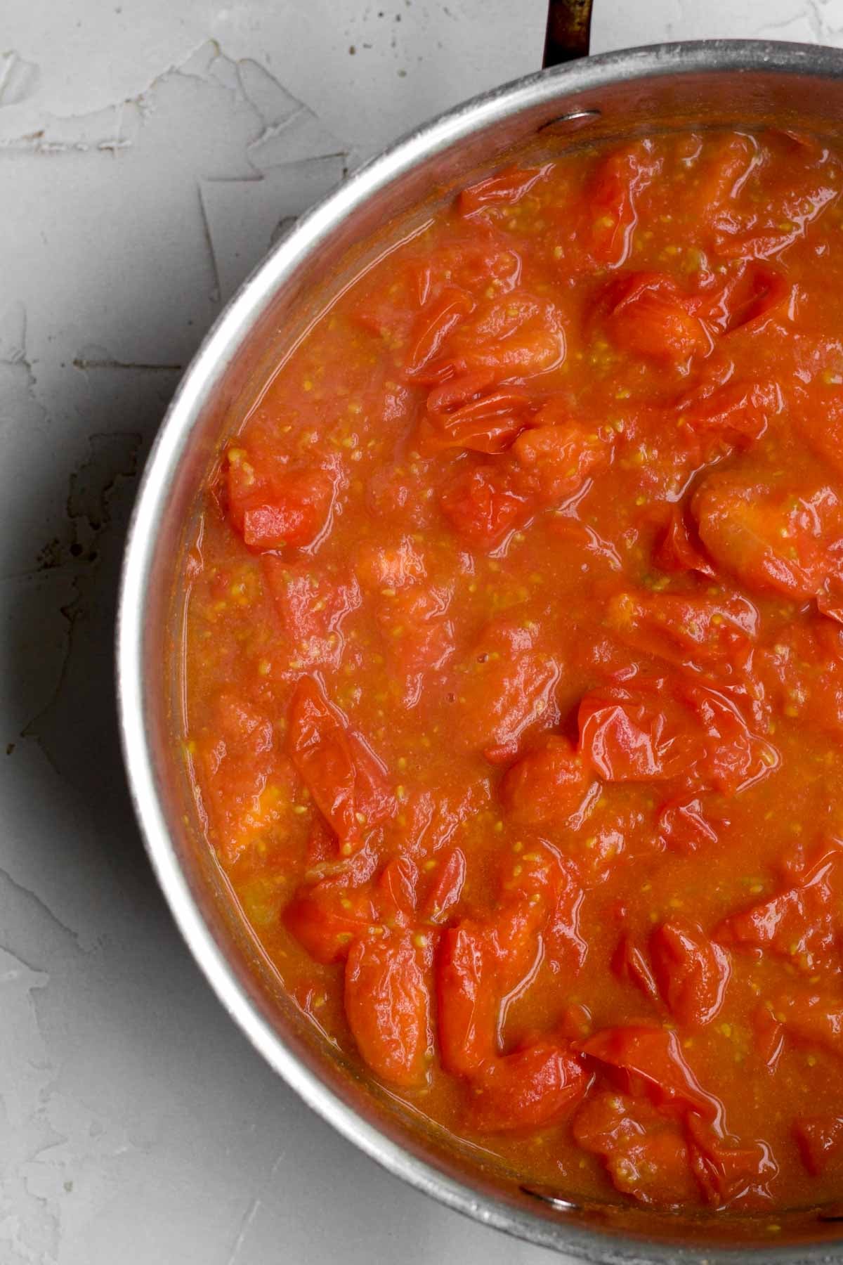 Heated broken-down tomatoes in a saucepan.