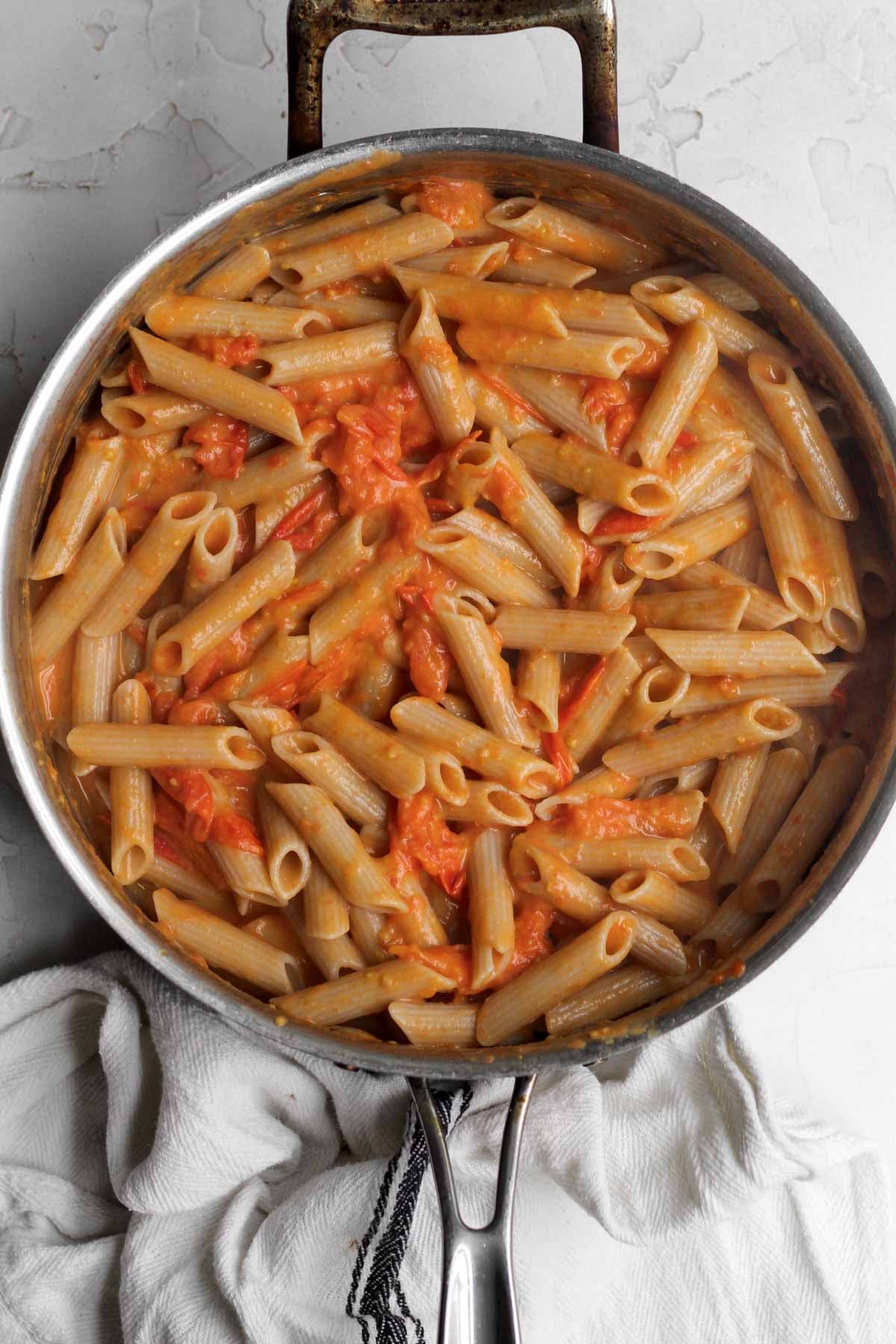 Mixing in cooked penne pasta into the tomato cream sauce.