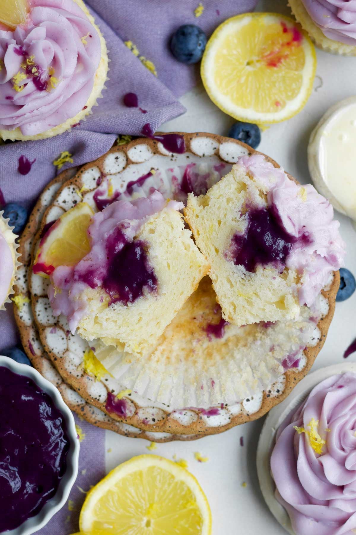 A halved, vibrant, lemon blueberry cupcake with gooey blueberry curd center rests on a plate.