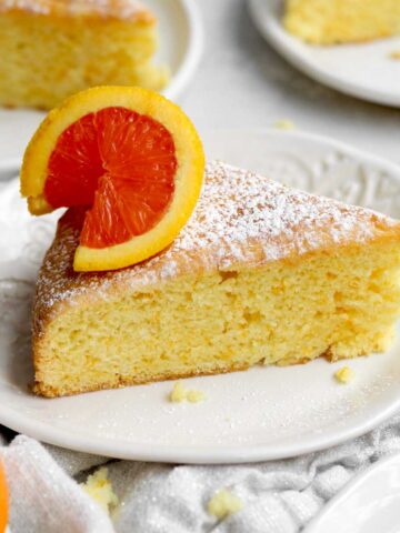 a tender slice of gluten-free orange cake dusted in sweet confectioner's sugar topped with fresh citrus.