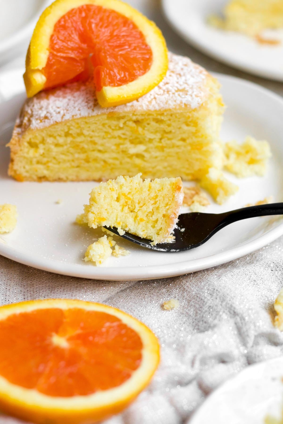 a fluffy, crumbly-textured bite of orange cake on a fork separated from a perfect slice.