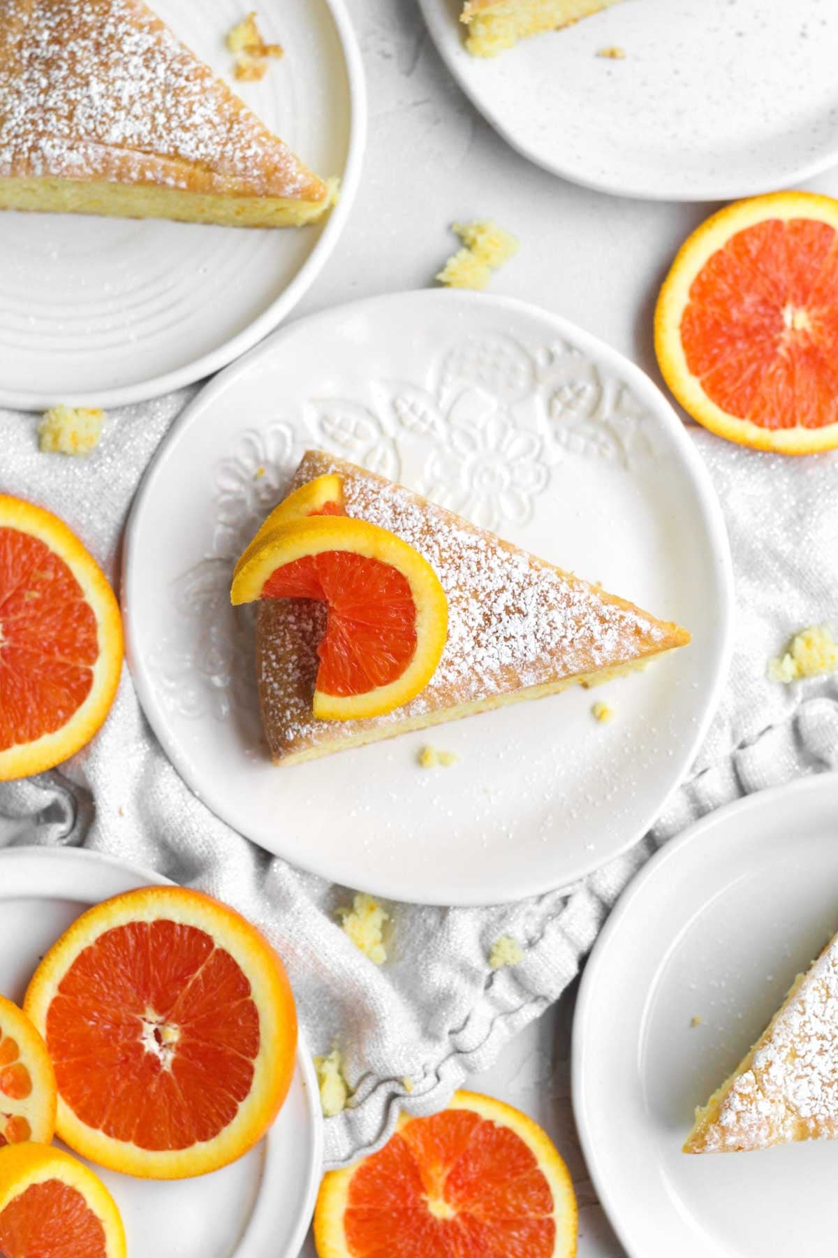 a triangular powdered sugared slice of orange cake topped with a vibrant round slice of citrus.