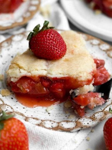 Gluten-free strawberry cobbler slice oozing with warm strawberry filling topped with a fresh strawberry.