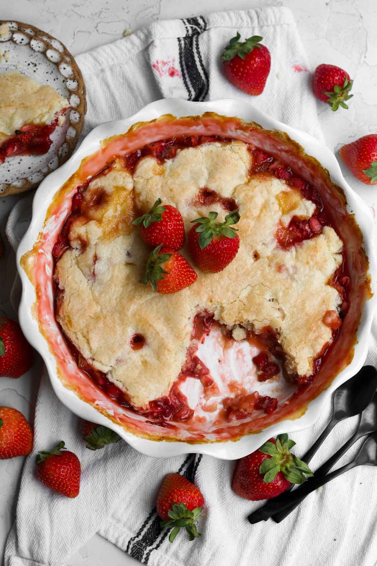 Strawberry cobbler in a baking dish with an eggless golden crust with a slice removed.