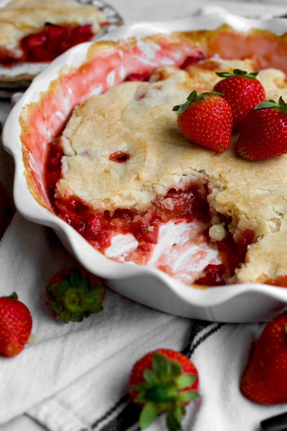 The removed slice of strawberry cobbler reveals a warm red fruity base layer protected by a golden crust.