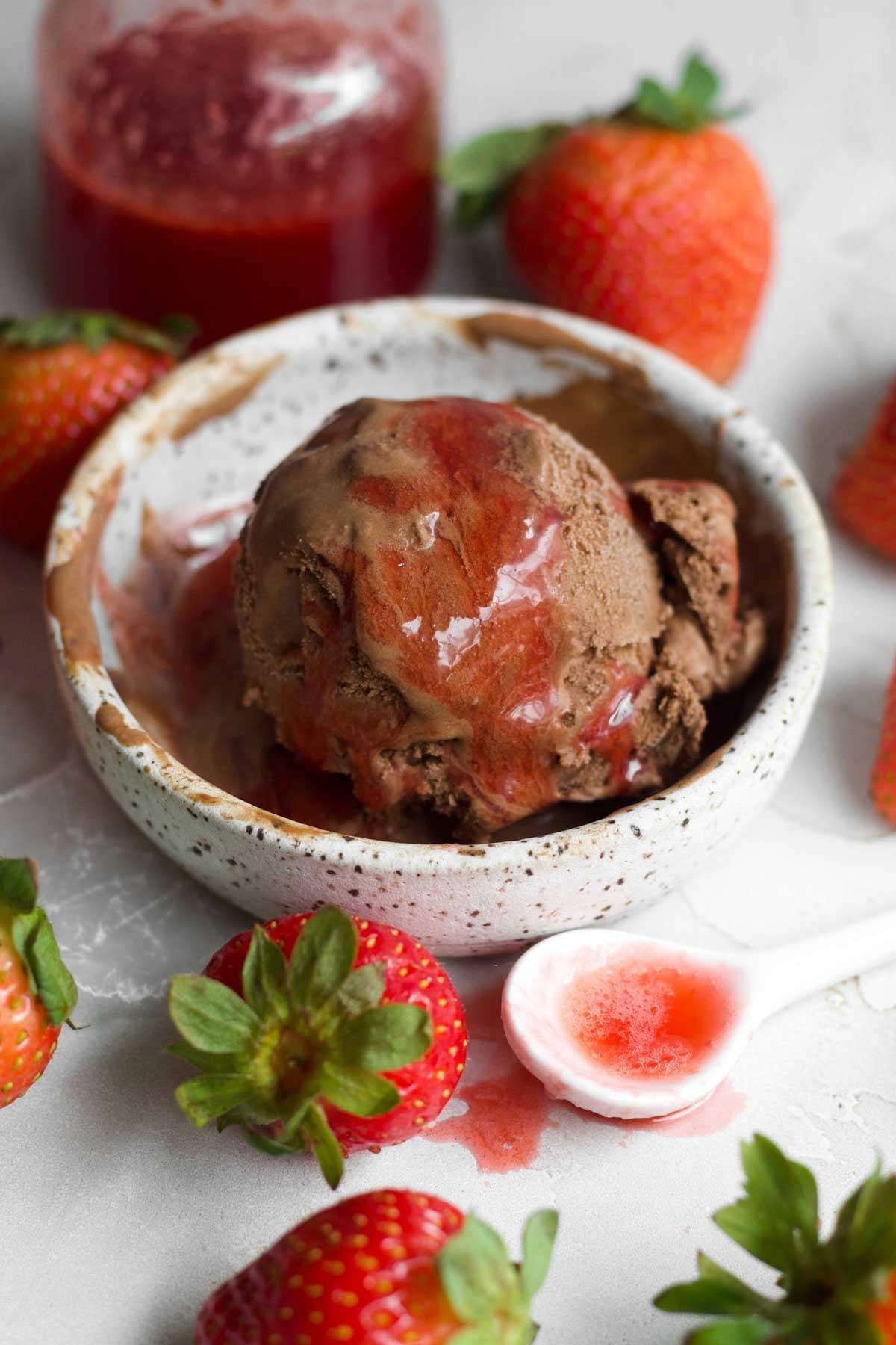 Glossy, rich red strawberry syrup cascades down the sides of rich chocolate ice cream in a bowl.