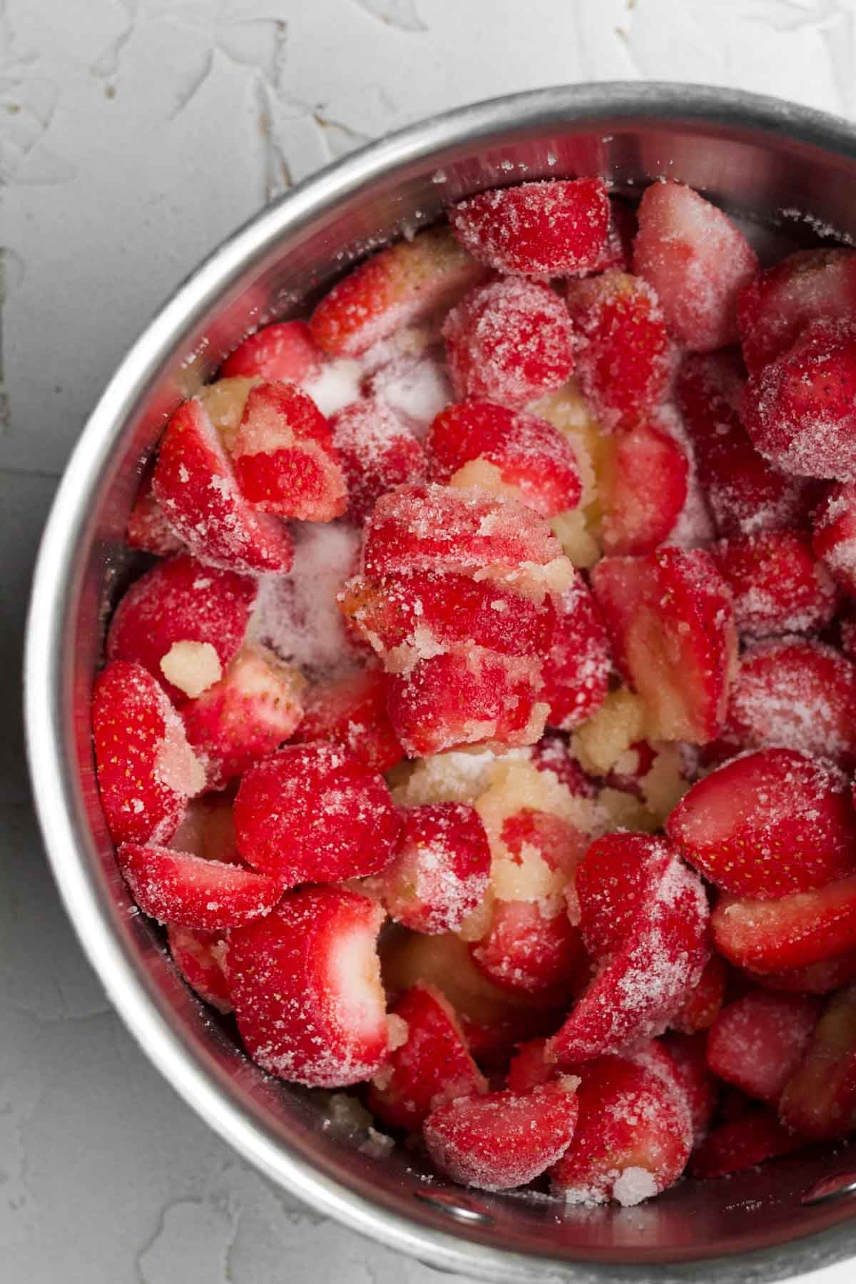A saucepan with the frozen strawberries, granulated sugar and orange juice mixed together.