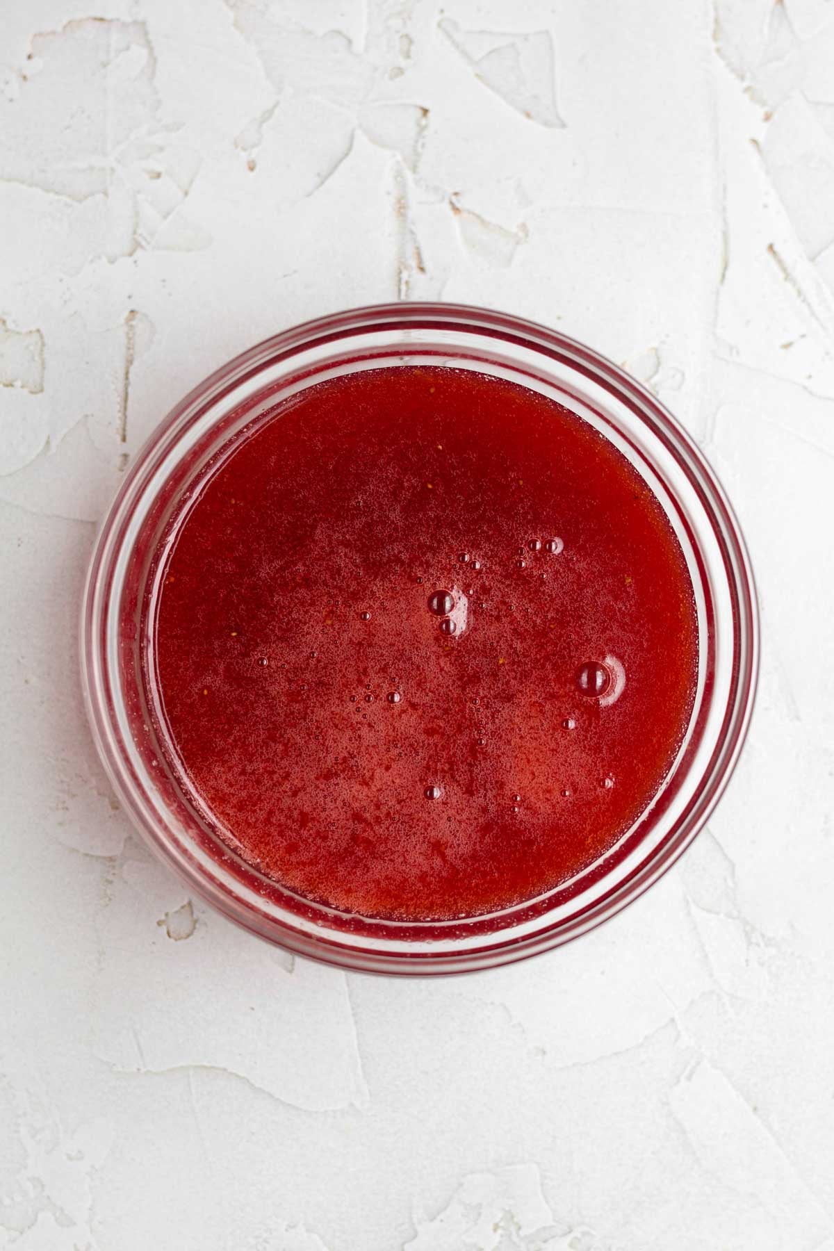 Strained sugary strawberry syrup in a glass bowl.
