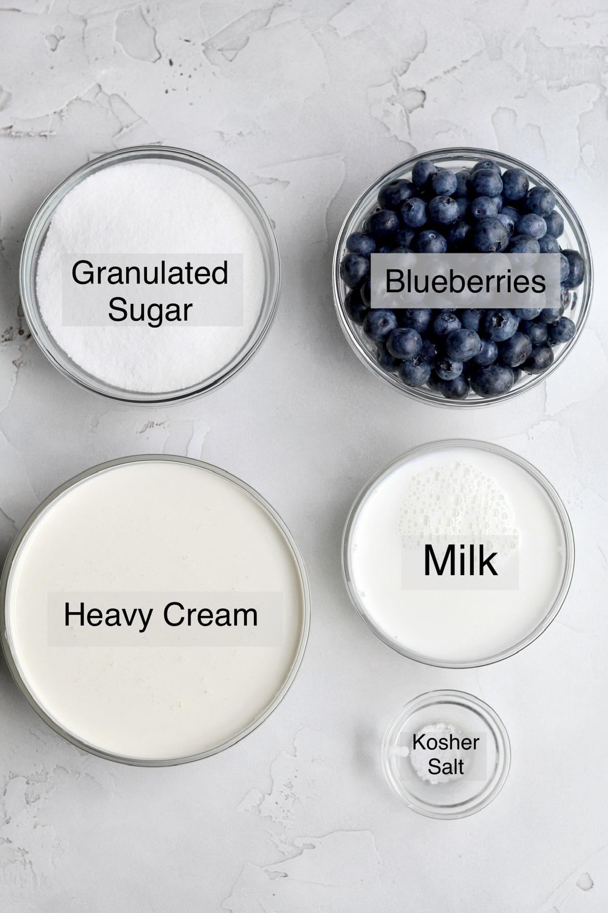 blueberry ice cream ingredients in separate bowls: granulated sugar, blueberries. heavy cream, milk, and kosher salt.