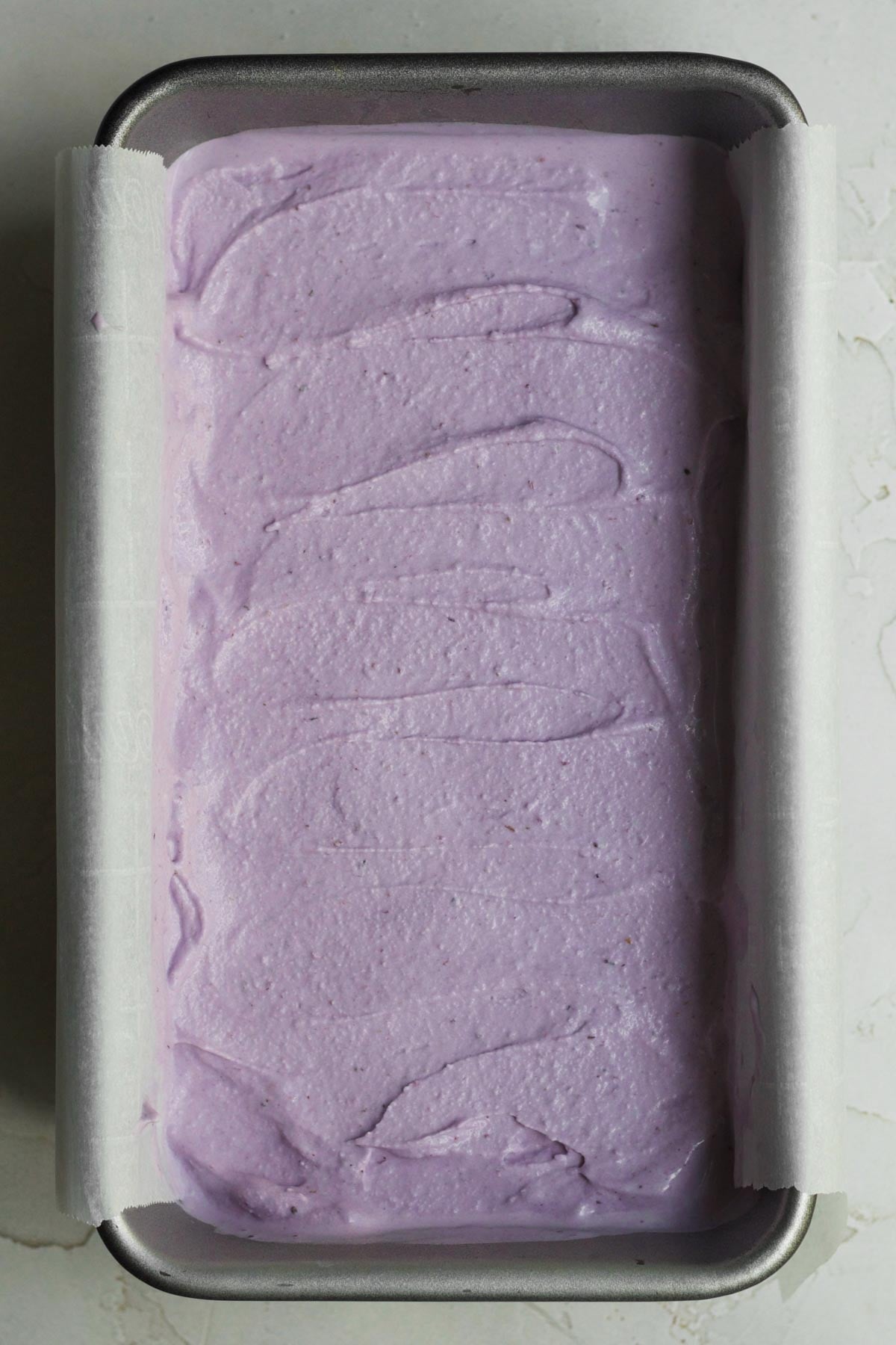 Filling a loaf pan with the blueberry ice cream liquid and smoothing the top.