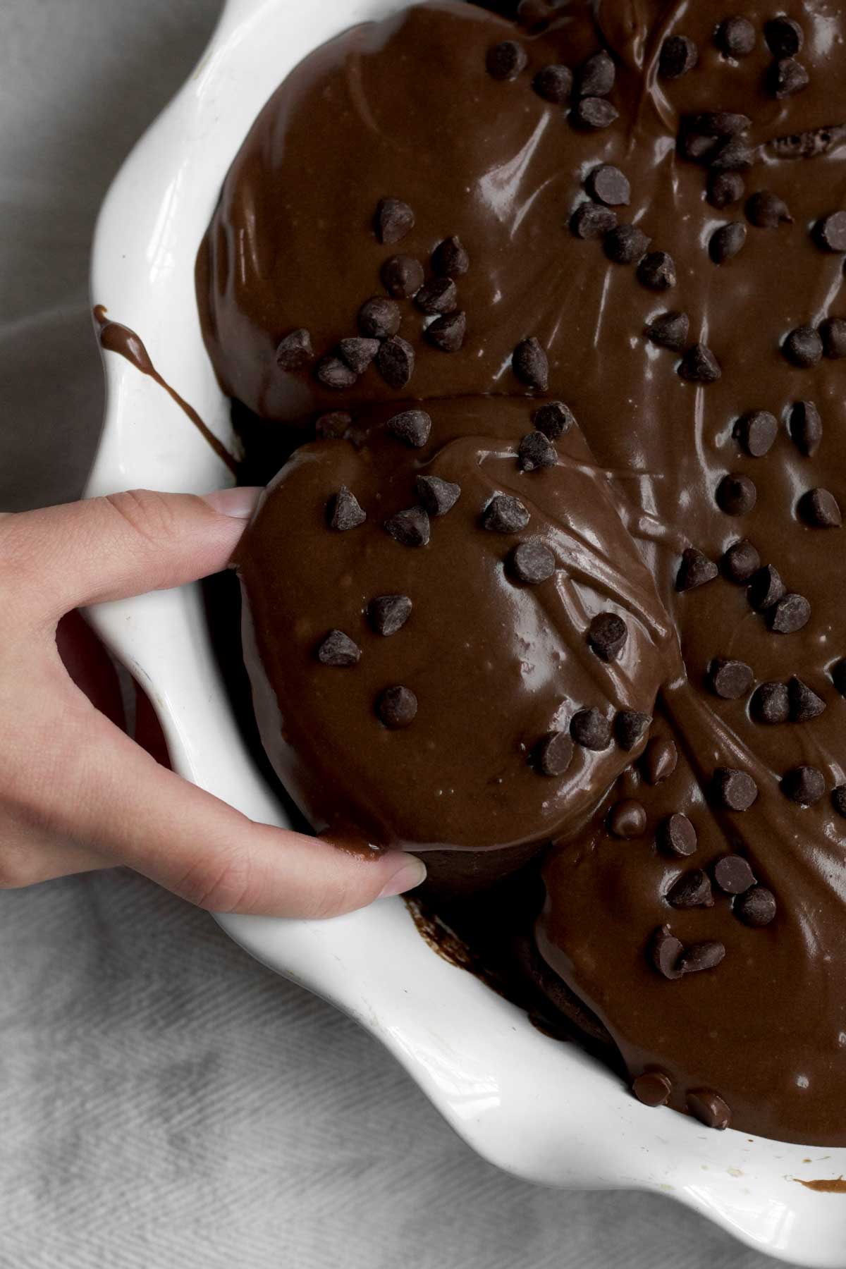 a hand carefully takes a delicious frosted chocolate cinnamon roll from a dish.