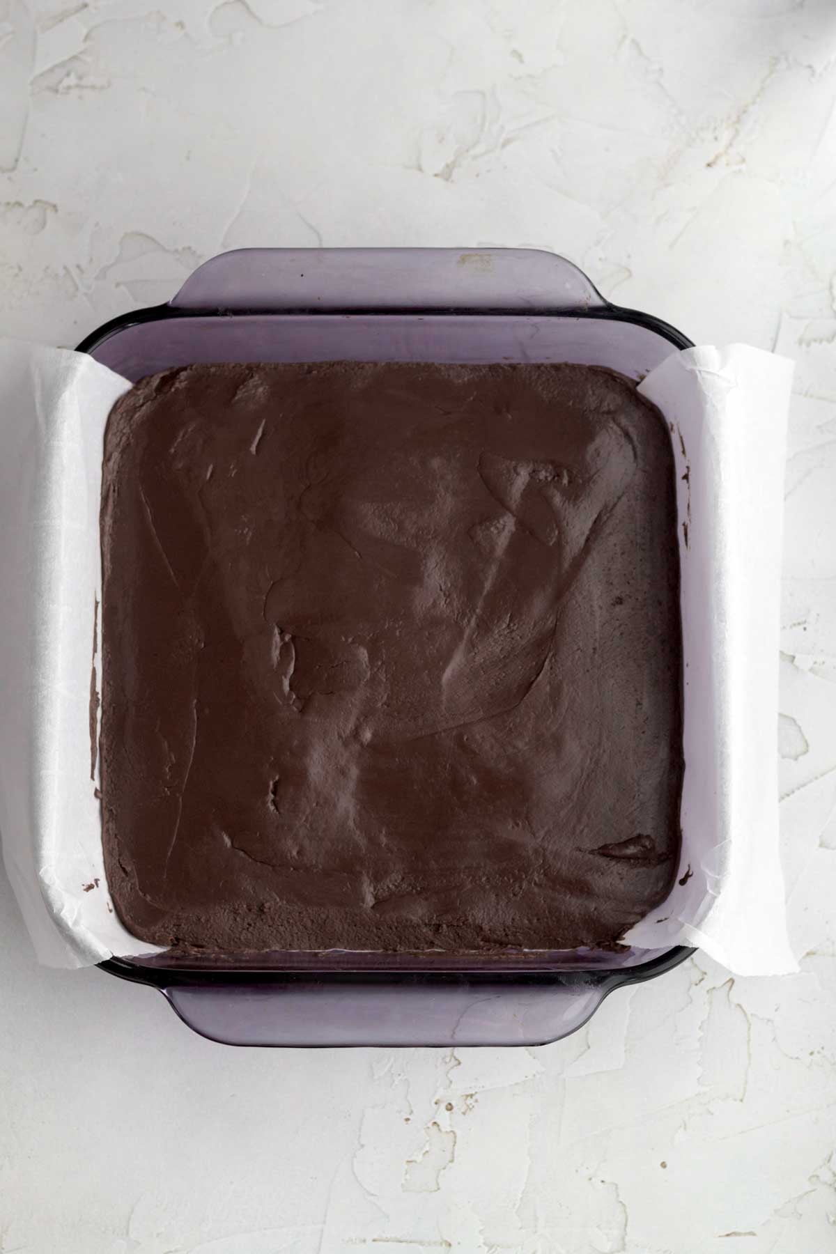 Filling a lined purple pan with the fudge and smoothing it out.
