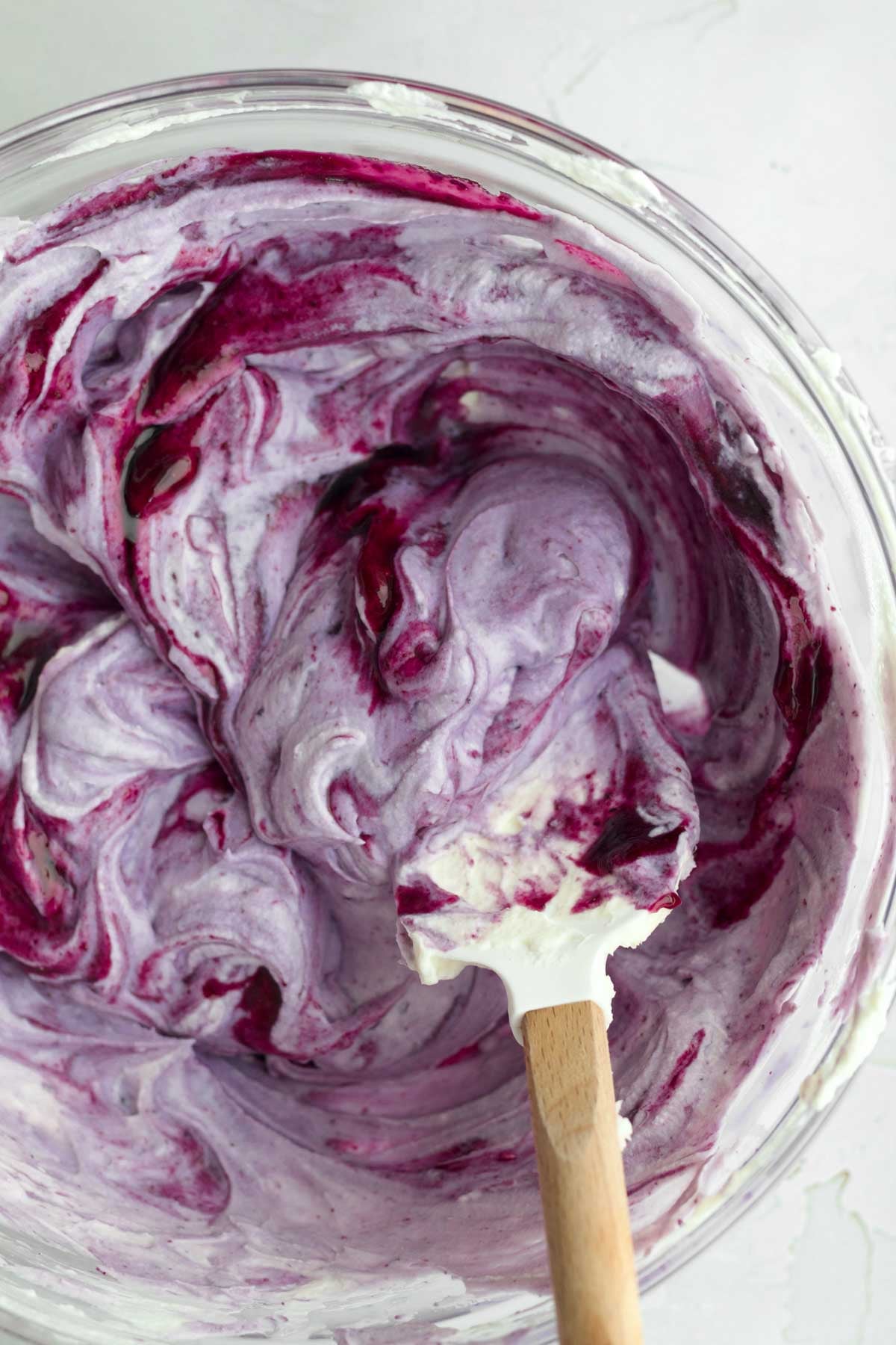 Mixing in deep violet blueberry liquid in a bowl.