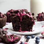 A halved chocolate blueberry muffin with its soft crumb interior with melted chocolate chips and bursted blueberries.