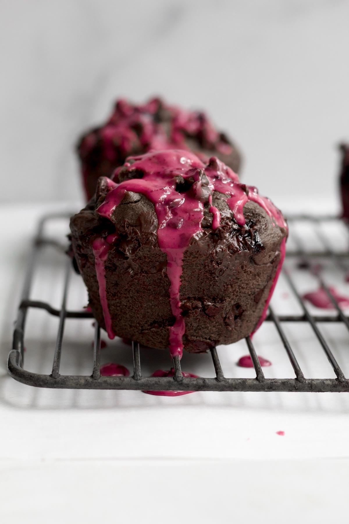 Thick, pink drizzle drips down the sides of the chocolate blueberry muffins.