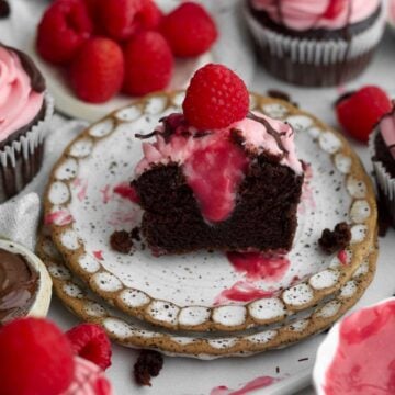 A chocolate raspberry cupcake halved exposing a thick drip of its raspberry curd filled center.