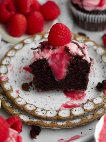 A chocolate raspberry cupcake halved exposing a thick drip of its raspberry curd filled center.