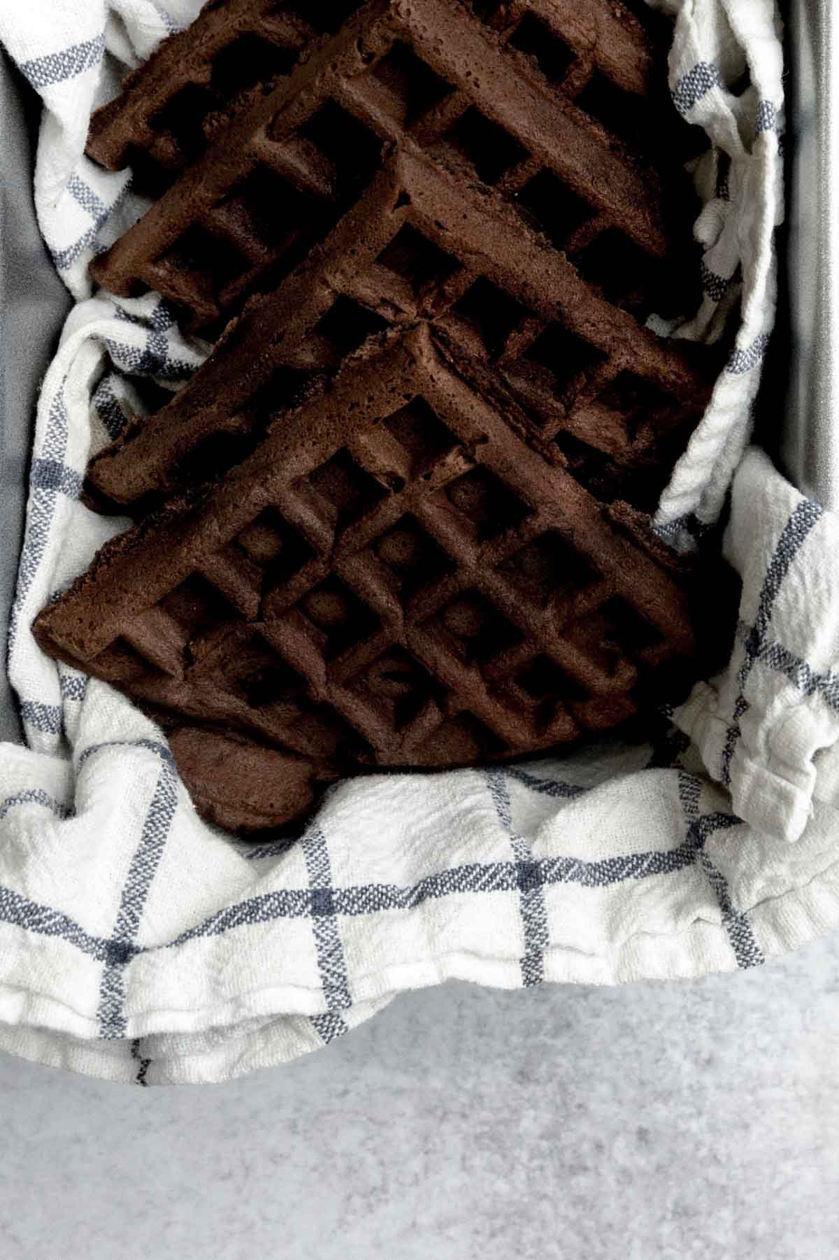 Fresh gluten-free chocolate waffles resting on a towel in a loaf pan.