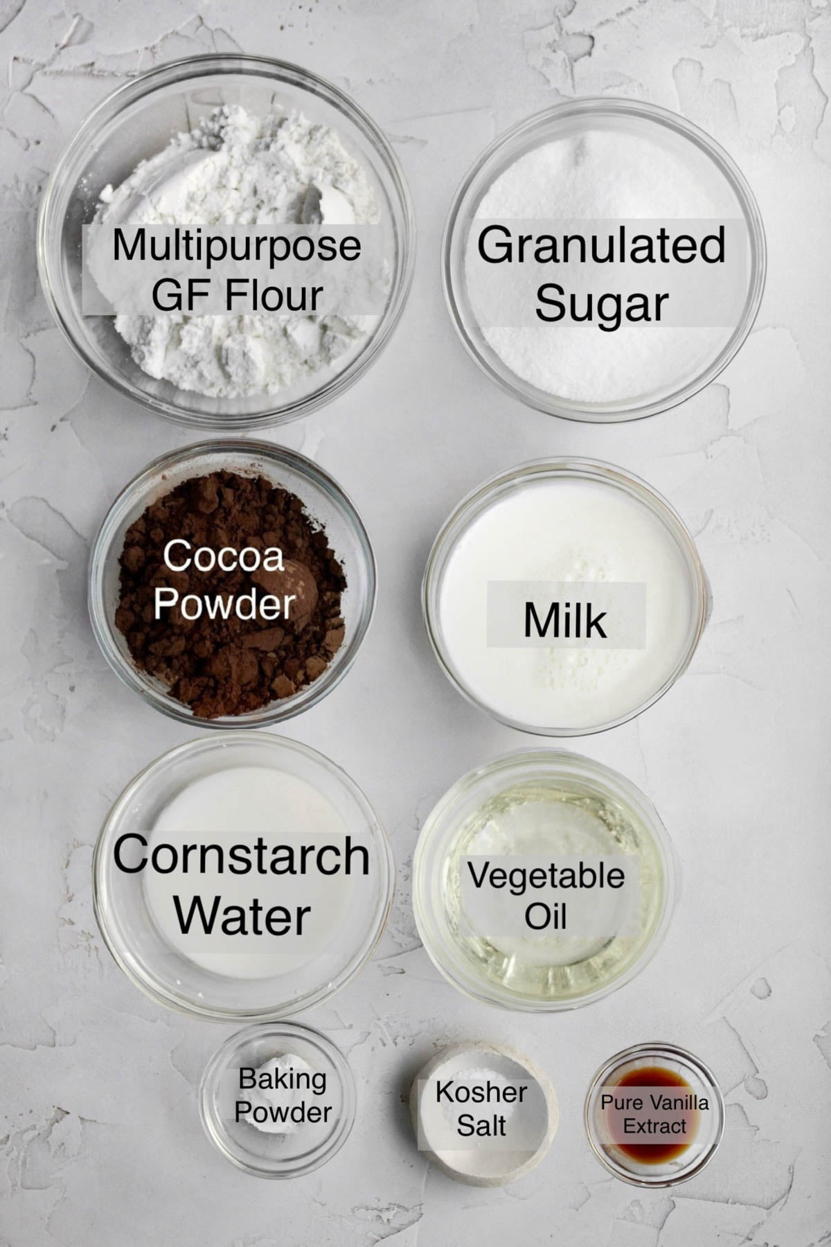 Chocolate waffles ingredients in separate bowls: multipurpose gluten free flour, granulated sugar, cocoa powder, milk, cornstarch water, vegetable oil, baking powder, kosher salt, and pure vanilla extract.