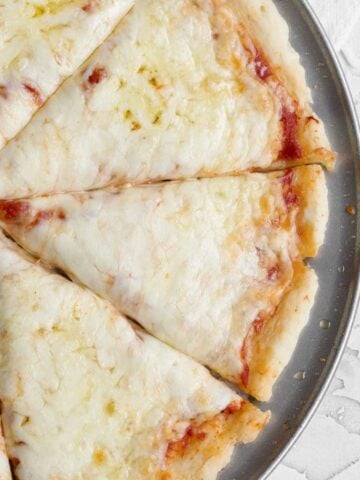 Slices of baked gluten free pizza dough topped with melted mozzarella cheese and red tomato sauce.