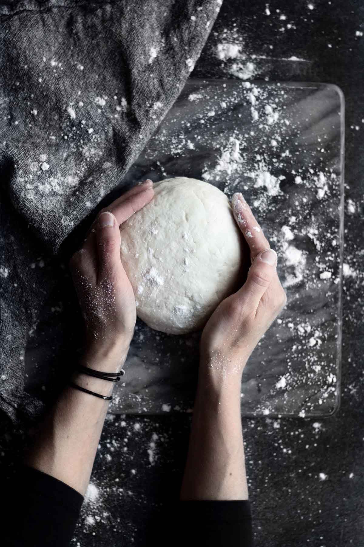 Flour covered hands shape the gluten free pizza dough into a healthy round ball.
