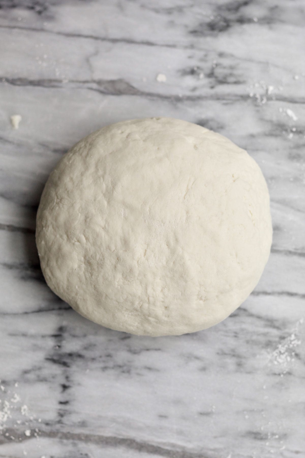 A smooth ball of proofed pizza dough on marble.