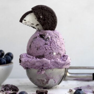 A scoop of purple Oreo blueberry ice cream topped with a halved gluten-free chocolate sandwich cookie.