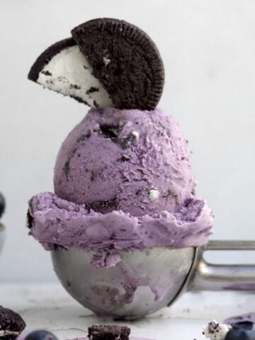 A scoop of purple Oreo blueberry ice cream topped with a halved gluten-free chocolate sandwich cookie.