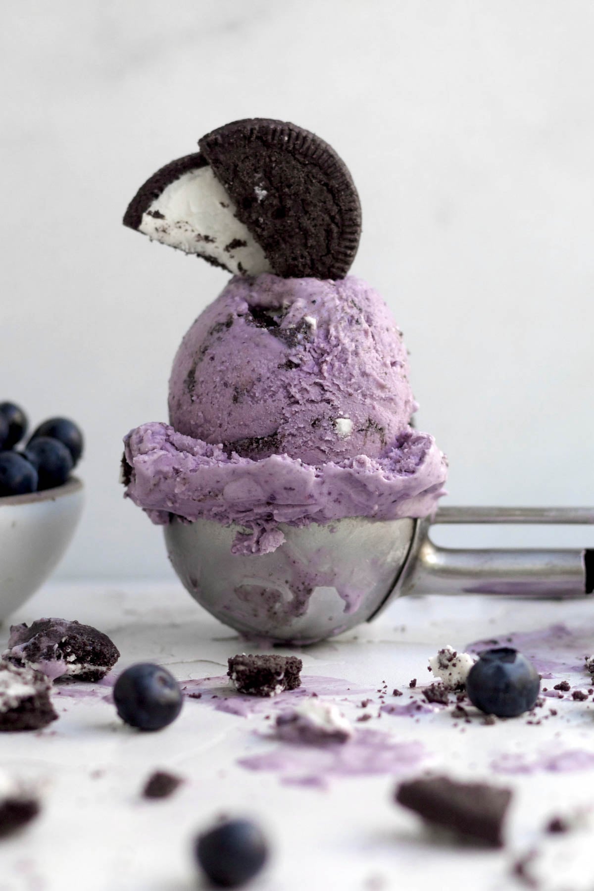 A scoop of purple Oreo blueberry ice cream topped with a halved gluten-free chocolate sandwich cookie.