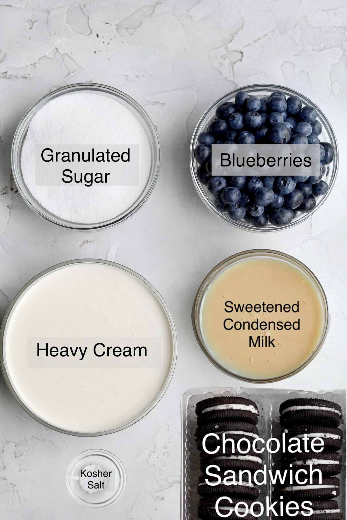 Oreo blueberry ice cream ingredients in separate containers: granulated sugar, blueberries, heavy cream, sweetened condensed milk, kosher salt and chocolate sandwich cookies.