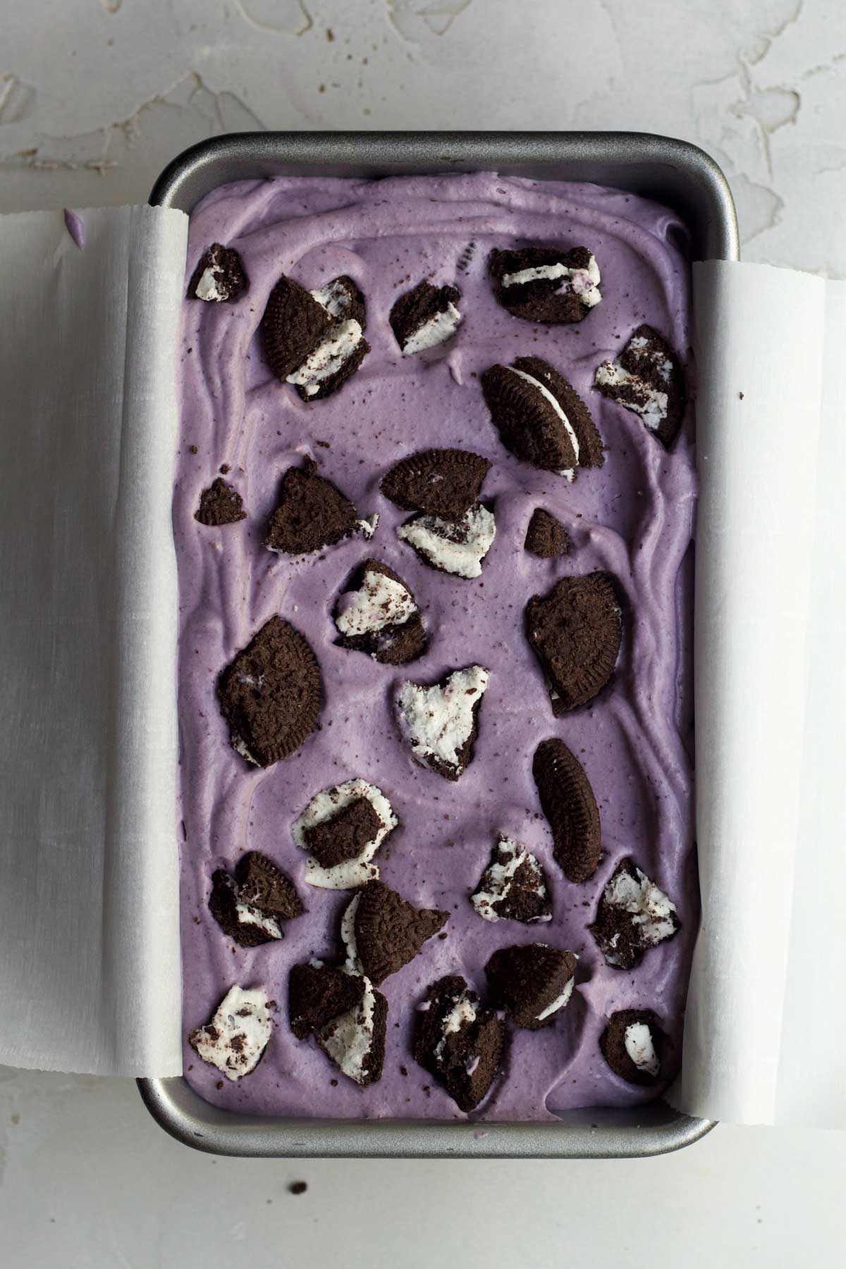 Filling a loaf pan with the ice cream and placing more broken sandwich cookies on top.