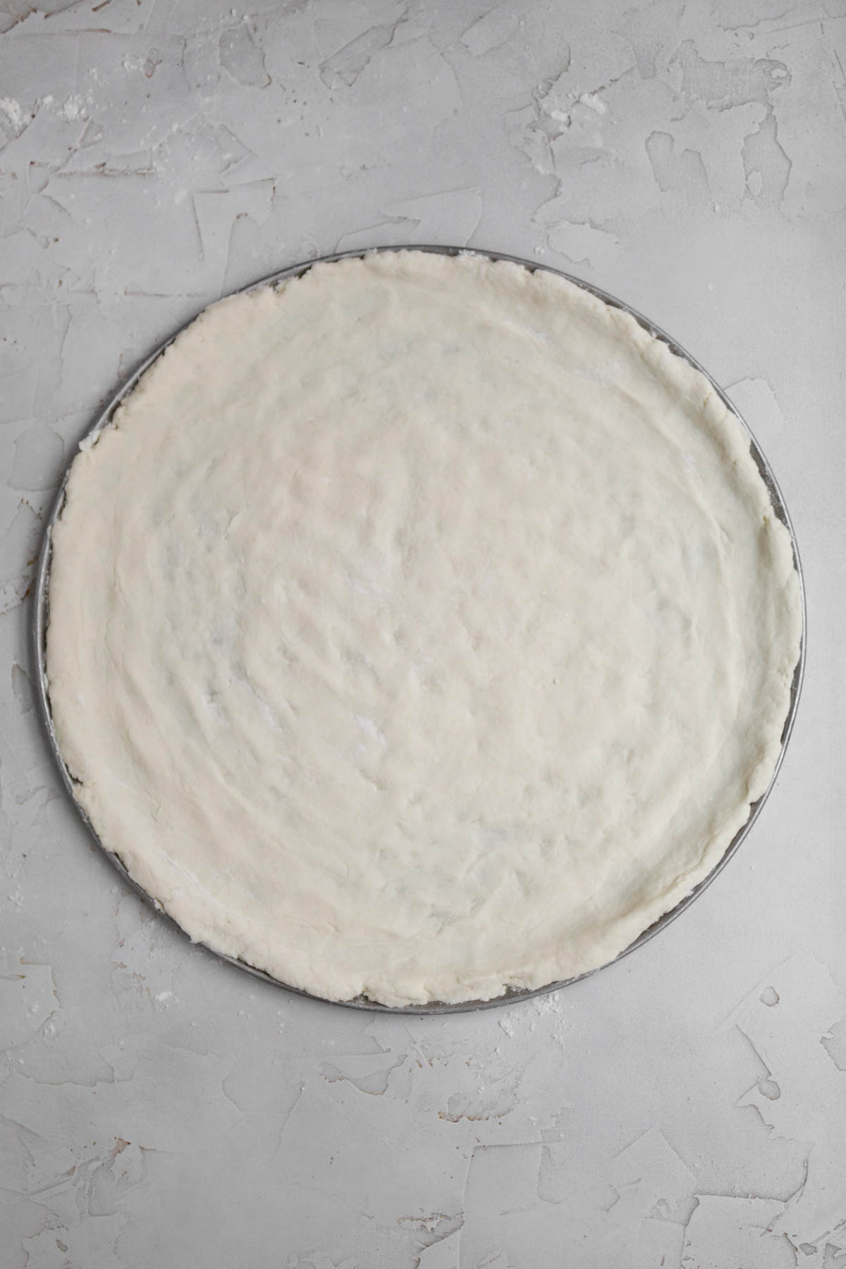 Raw gluten free pizza dough on pressed onto a pizza pan.