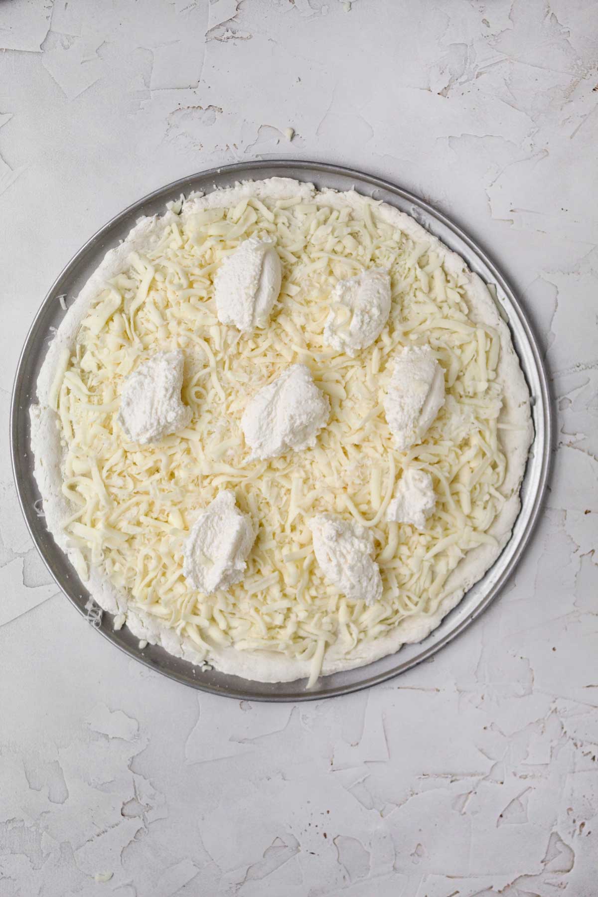 Topping the pizza crust with mozzarella cheese and ricotta.