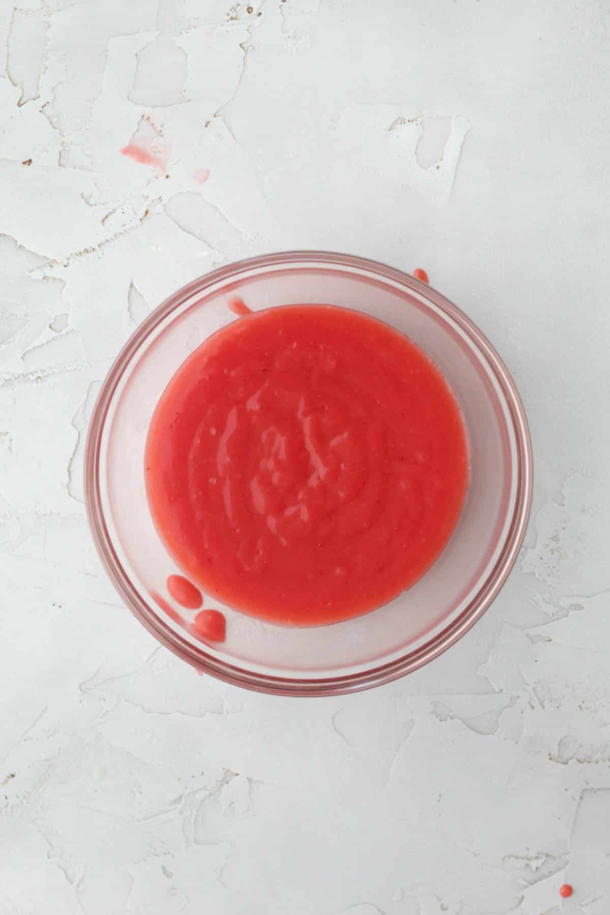 Strained bright strawberry curd in a glass bowl.