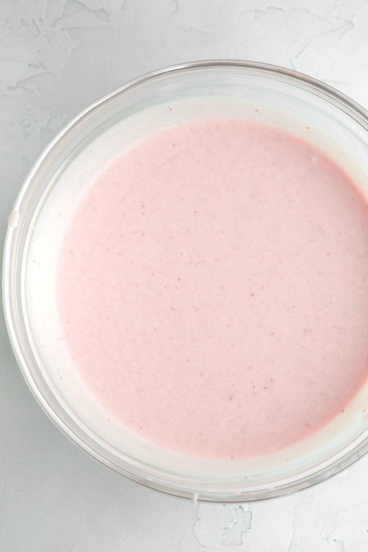 Pink, strained strawberry ice cream base in a glass bowl.