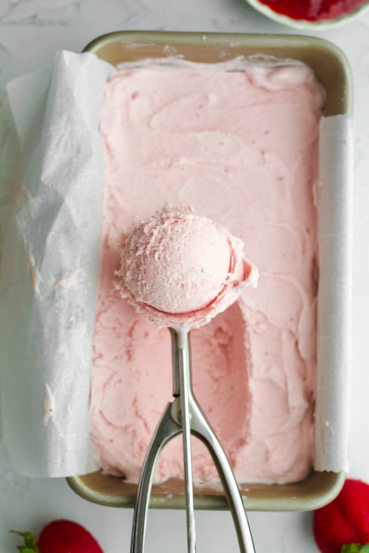 A scoop of creamy frozen strawberry ice cream held over a pan.