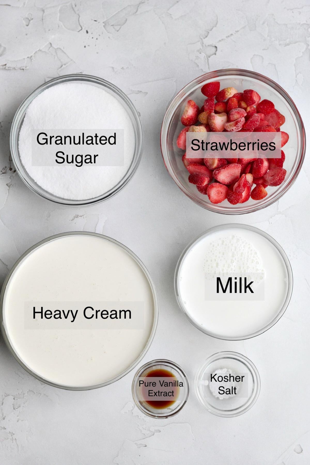 Strawberry ice cream ingredients in separate bowls: granulated sugar, strawberries, heavy cream, milk, pure vanilla extract, and kosher salt.