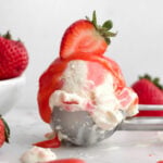 A perfect scoop of strawberry swirl ice cream topped with luscious strawberry curd and a halved strawberry.