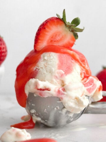 A perfect scoop of strawberry swirl ice cream topped with luscious strawberry curd and a halved strawberry.