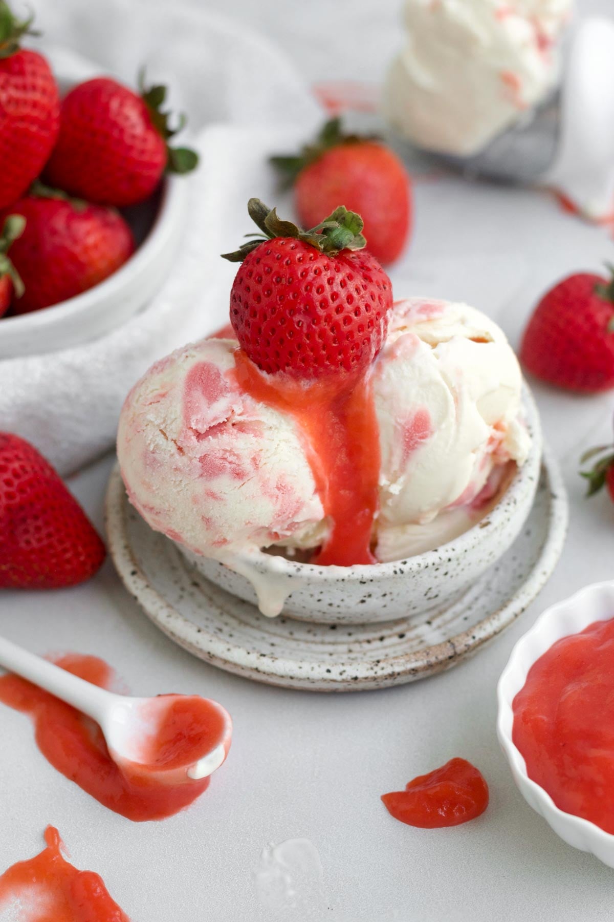 A bowl of strawberry swirl ice cream with a thick strawberry curd drizzle and a whole strawberry.