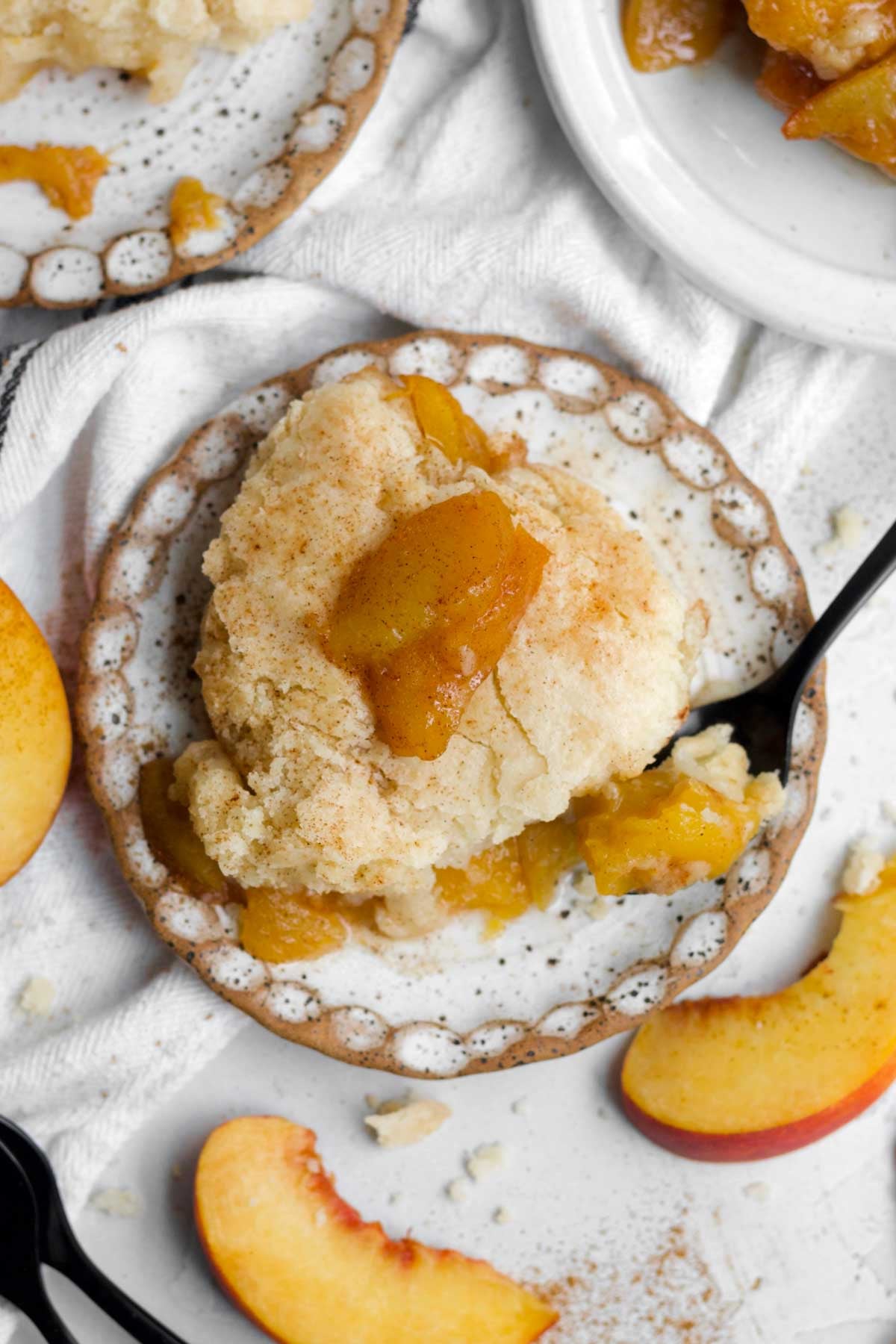 A golden slice of gluten free peach cobbler topped with a glistening baked peach.