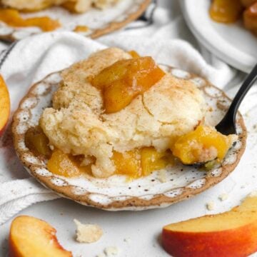 A cozy, warm slice of gluten free peach cobbler resting on a rustic plate with a fork.