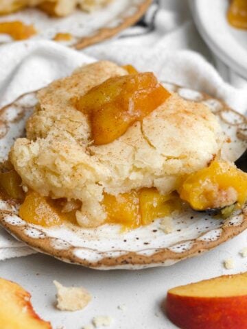 A cozy, warm slice of gluten free peach cobbler resting on a rustic plate with a fork.