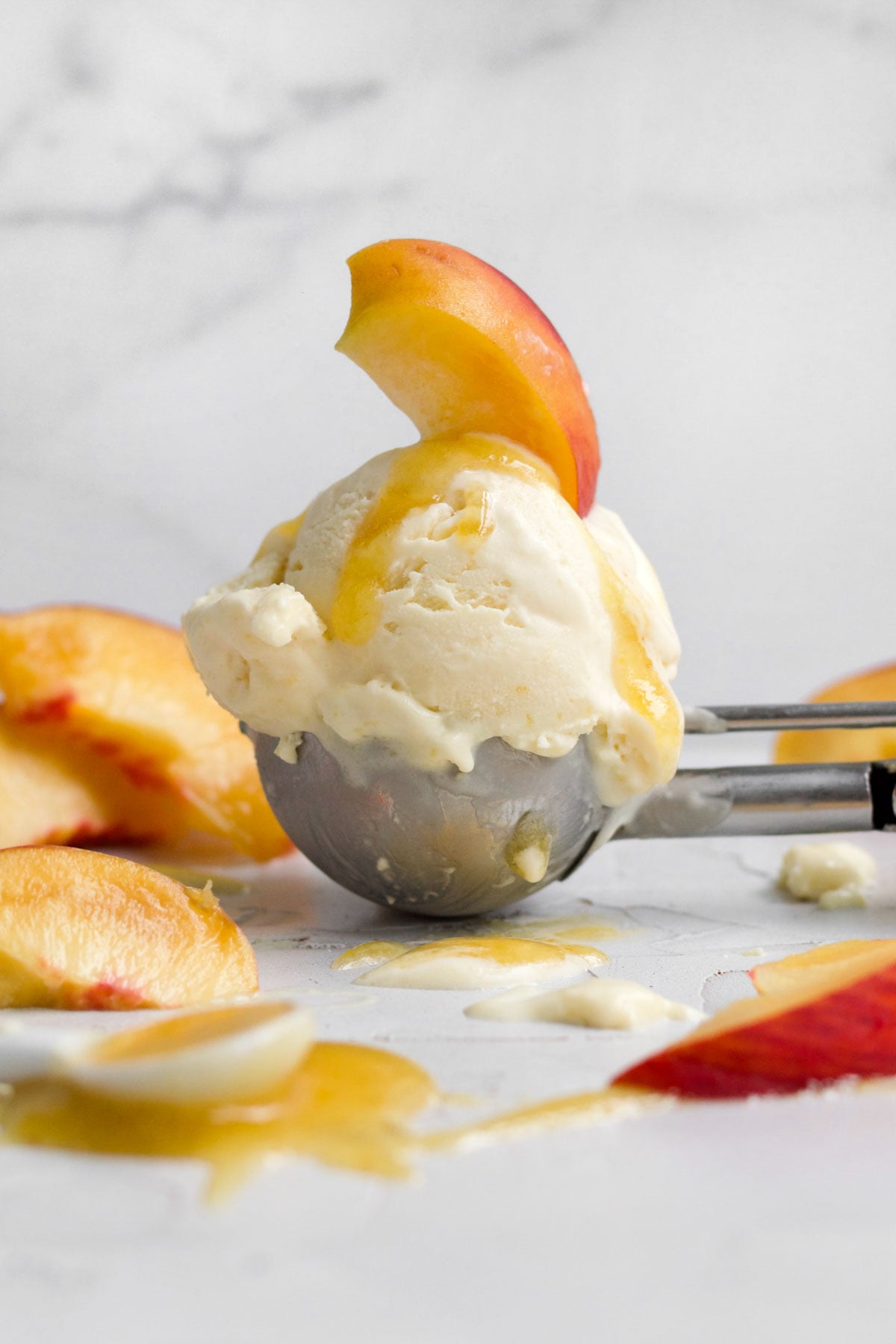 Solitary scoop of creamy peach ice cream topped with a fresh peach slice and peach syrup.