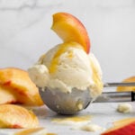 Solitary scoop of creamy peach ice cream topped with a fresh peach slice and peach syrup.