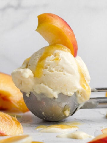 Solitary scoop of creamy peach ice cream topped with a fresh peach slice and peach syrup.