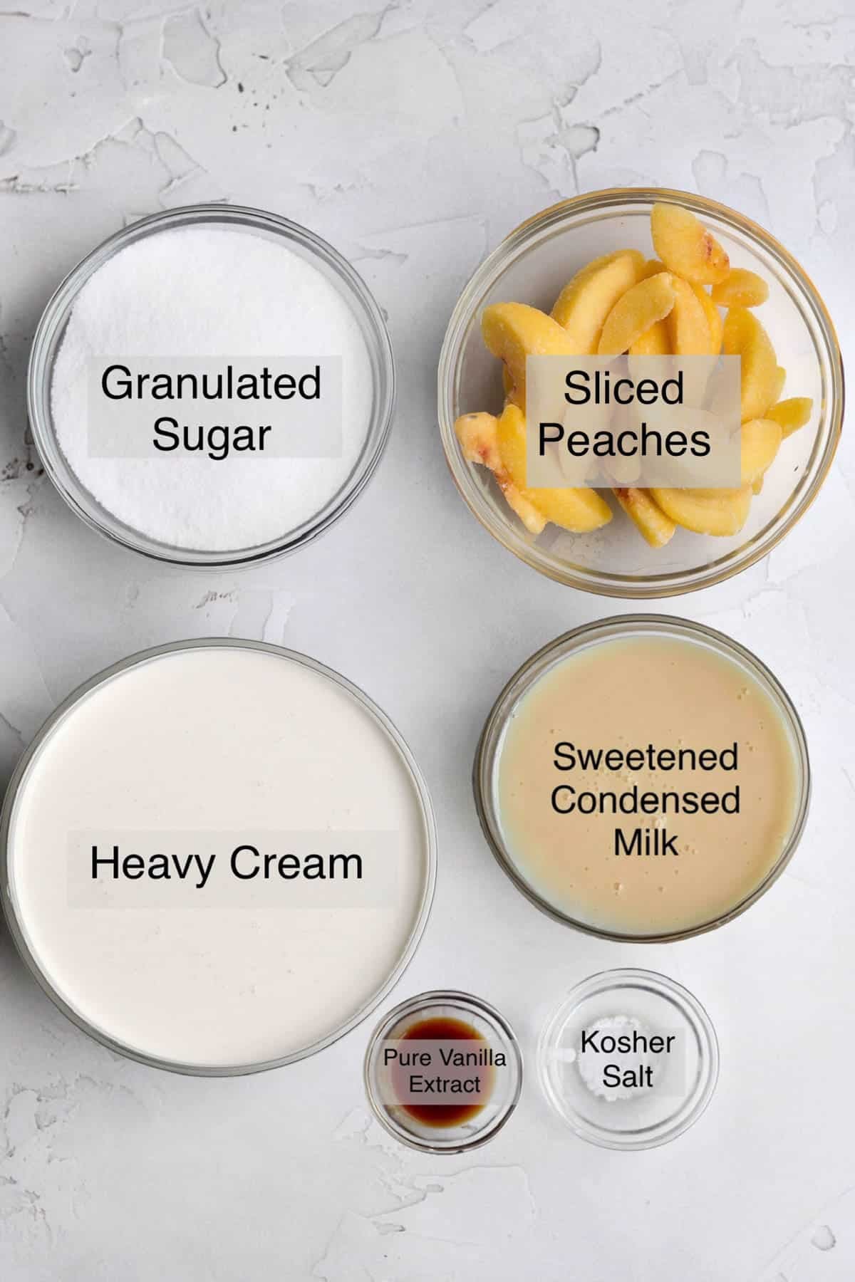 Peach ice cream ingredients in separate bowls: Granulated sugar, sliced peaches, heavy cream, sweetened condensed milk, pure vanilla extract, and kosher salt.