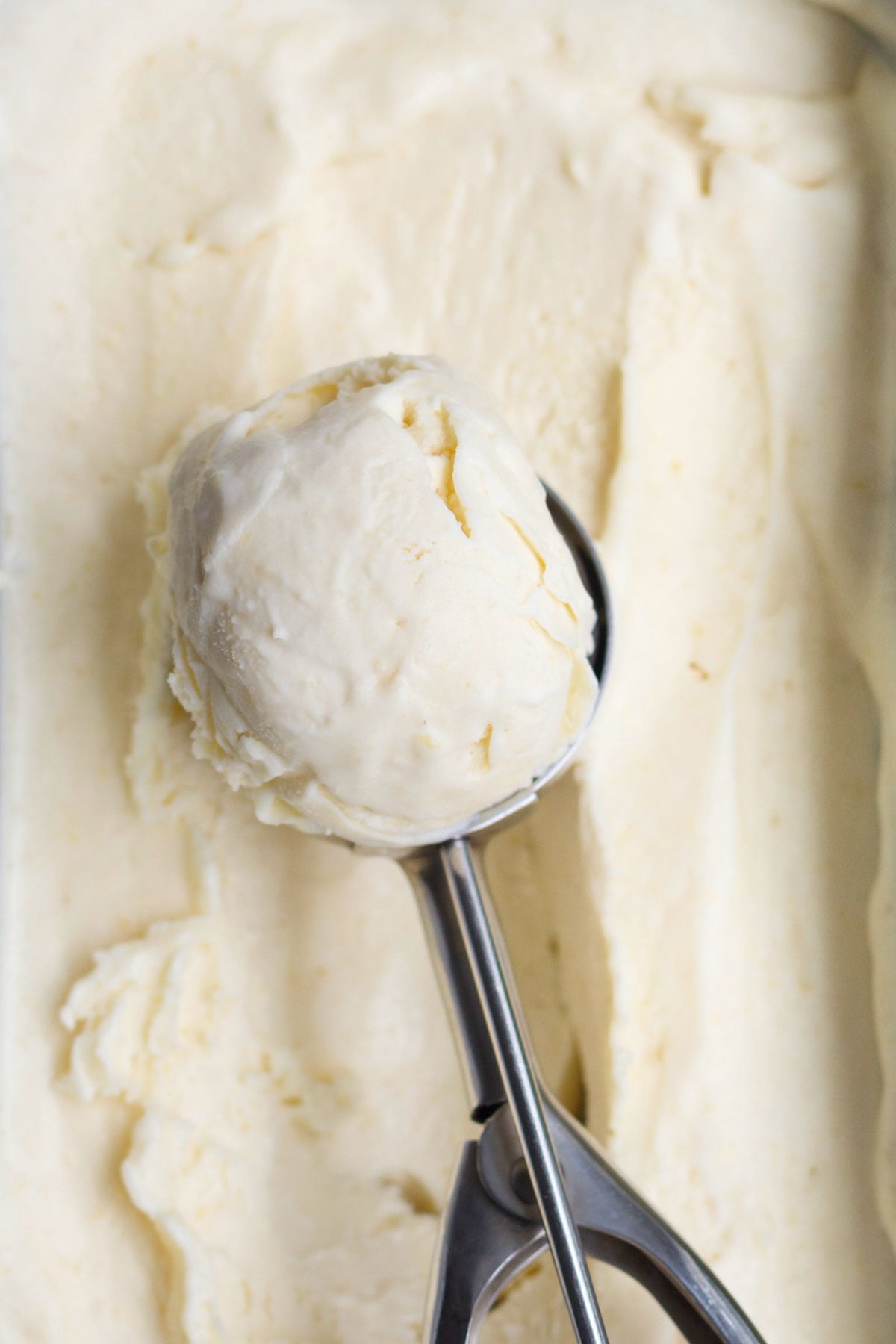 Freshly frozen peach ice cream in a loaf pan with a scoop.