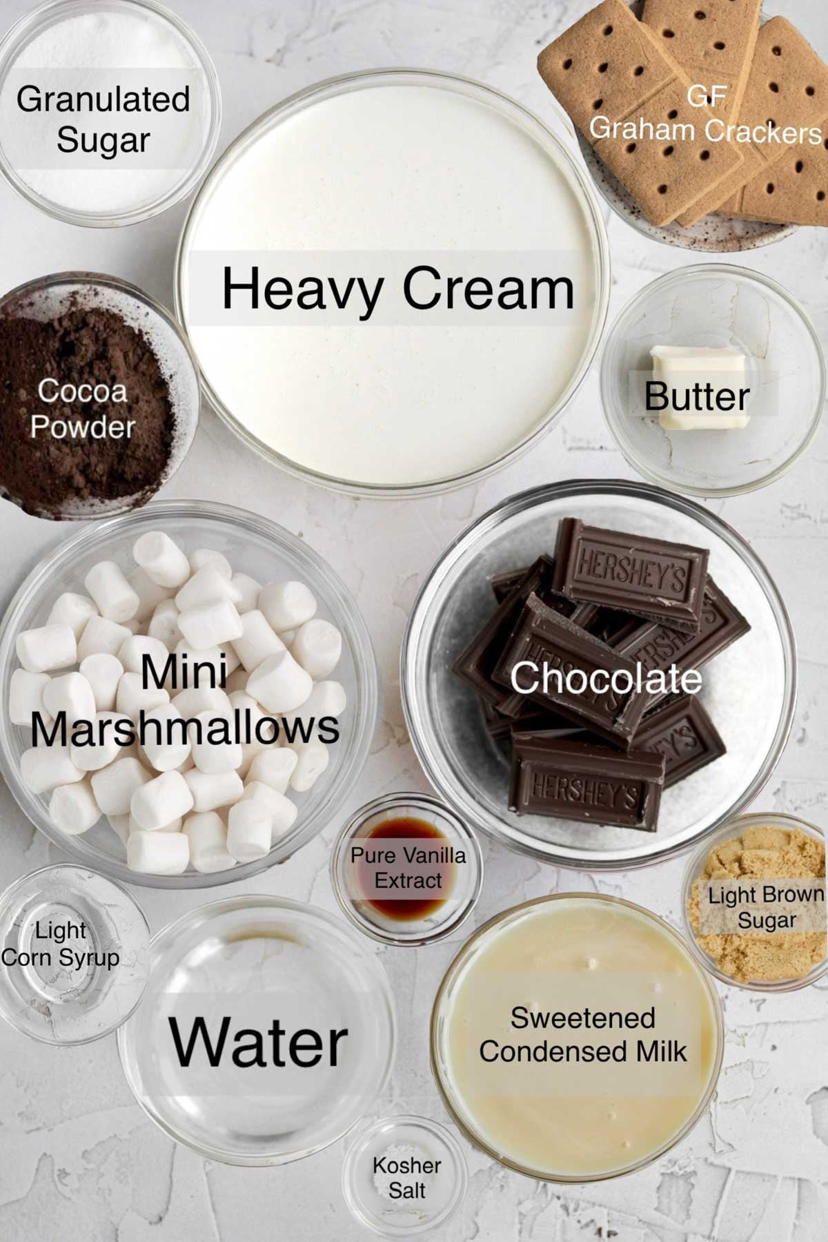 S'mores ice cream ingredients in separate bowls: granulated sugar, heavy cream, gluten free graham crackers, cocoa powder, butter, mini marshmallows, chocolate, light corn syrup, pure vanilla extract, light brown sugar, water, sweetened condensed milk and kosher salt.